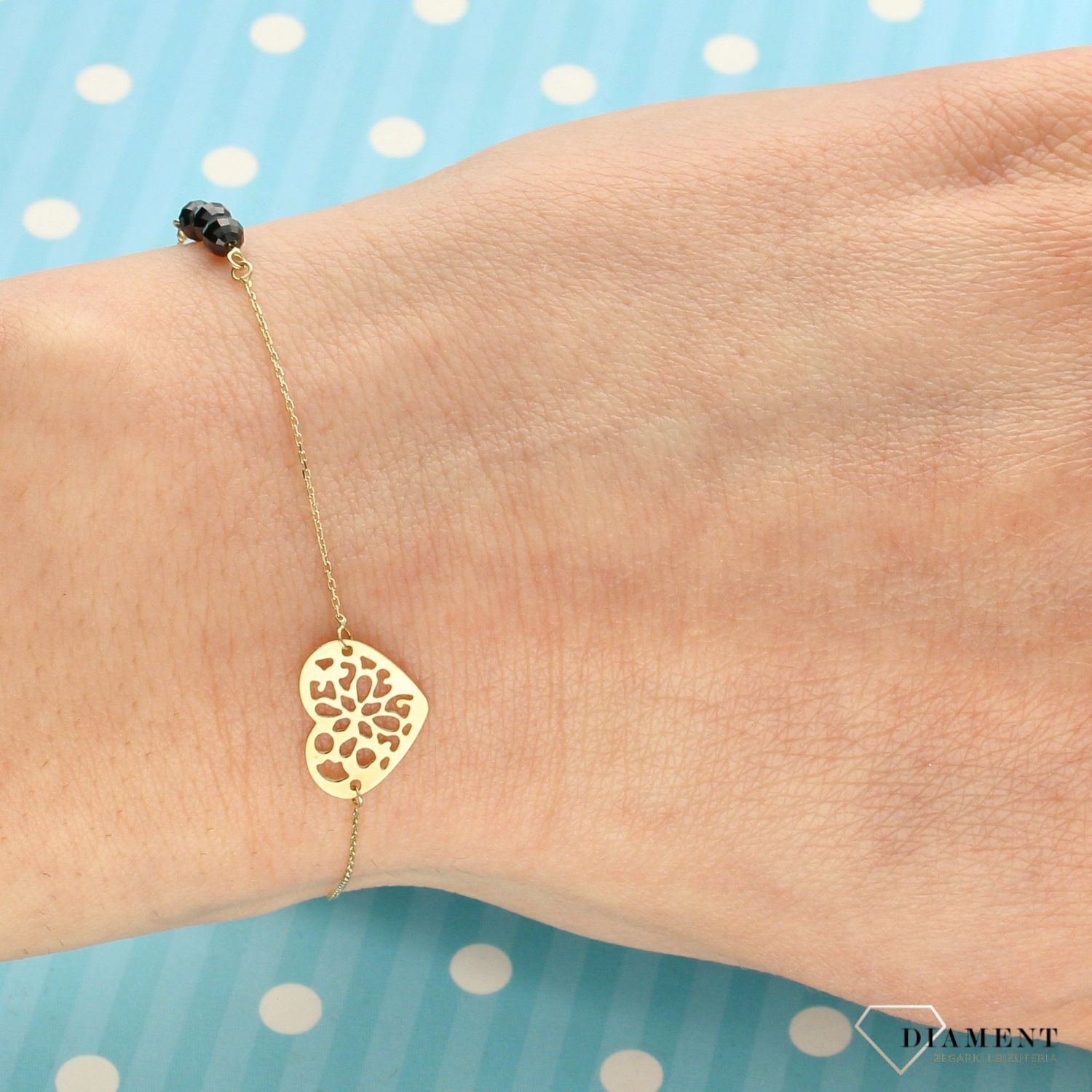 Złota bransoletka celebrytka na delikatnym łańcuszku ozdobiona została zawieszką w kształcie ażurkowego serca oraz trzech czarnych koralików. Zapraszamy!  (1).jpg