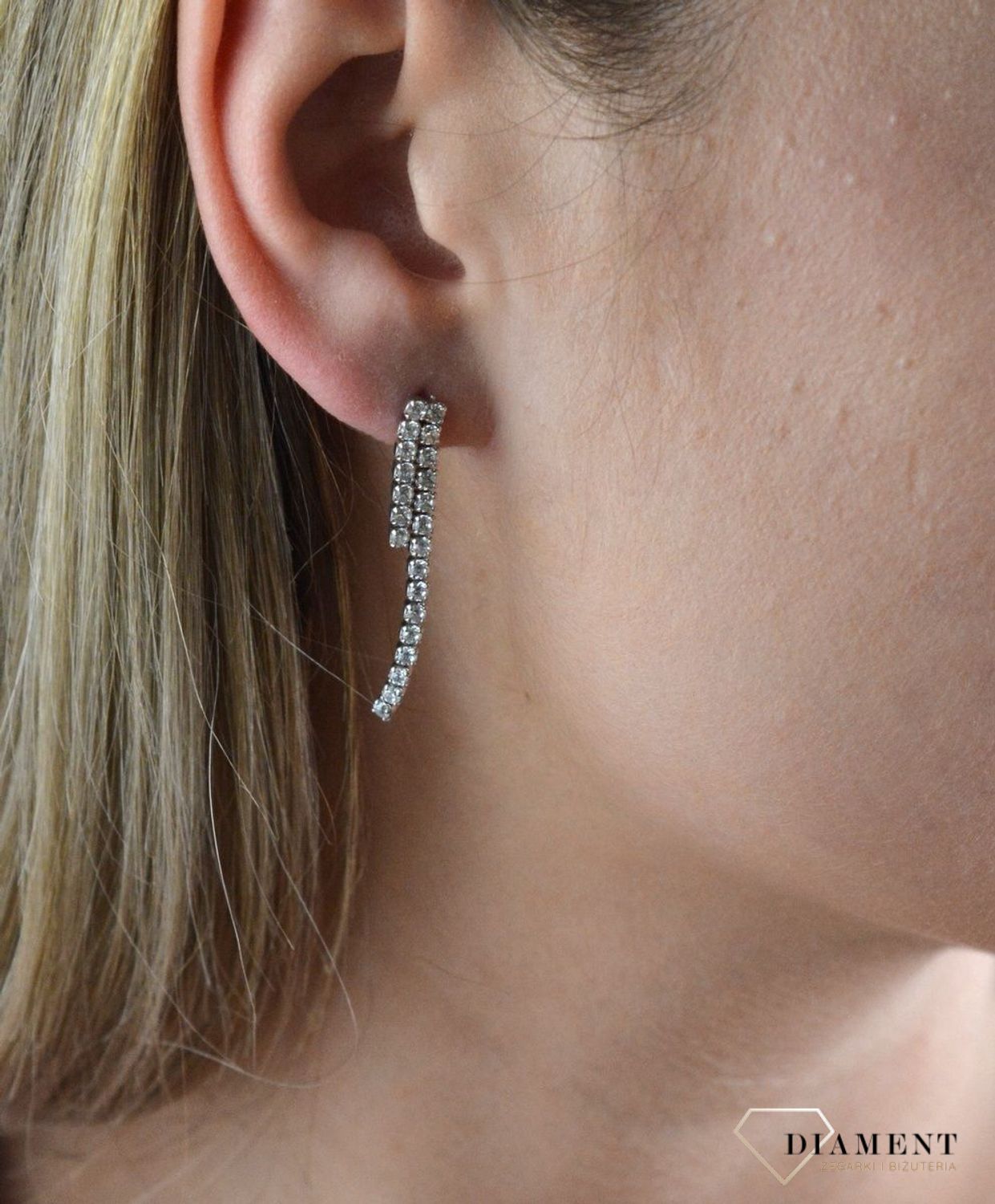 Srebrne kolczyki wiszące wtłoczone pasmem cyrkonii 27102510. Świetny dodatek do wielu stylizacji, zarówno tych codziennych, jak i na ważne okazje. Ten wzór kolczyka ma ponadczasowy kształt i wzór. To wykończenie nadaje całości.jpg