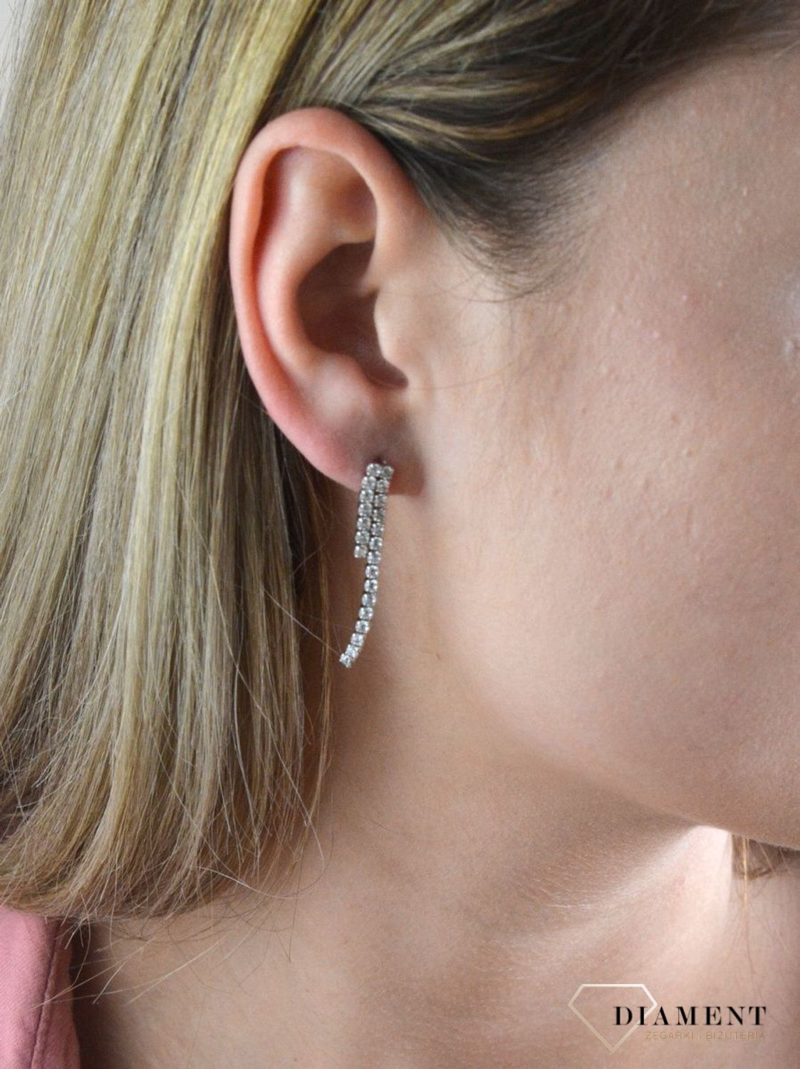 Srebrne kolczyki wiszące wtłoczone pasmem cyrkonii 27102510. Świetny dodatek do wielu stylizacji, zarówno tych codziennych, jak i na ważne okazje. Ten wzór kolczyka ma ponadczasowy kształt i wzór. To wykończenie nadaje całości.jpg