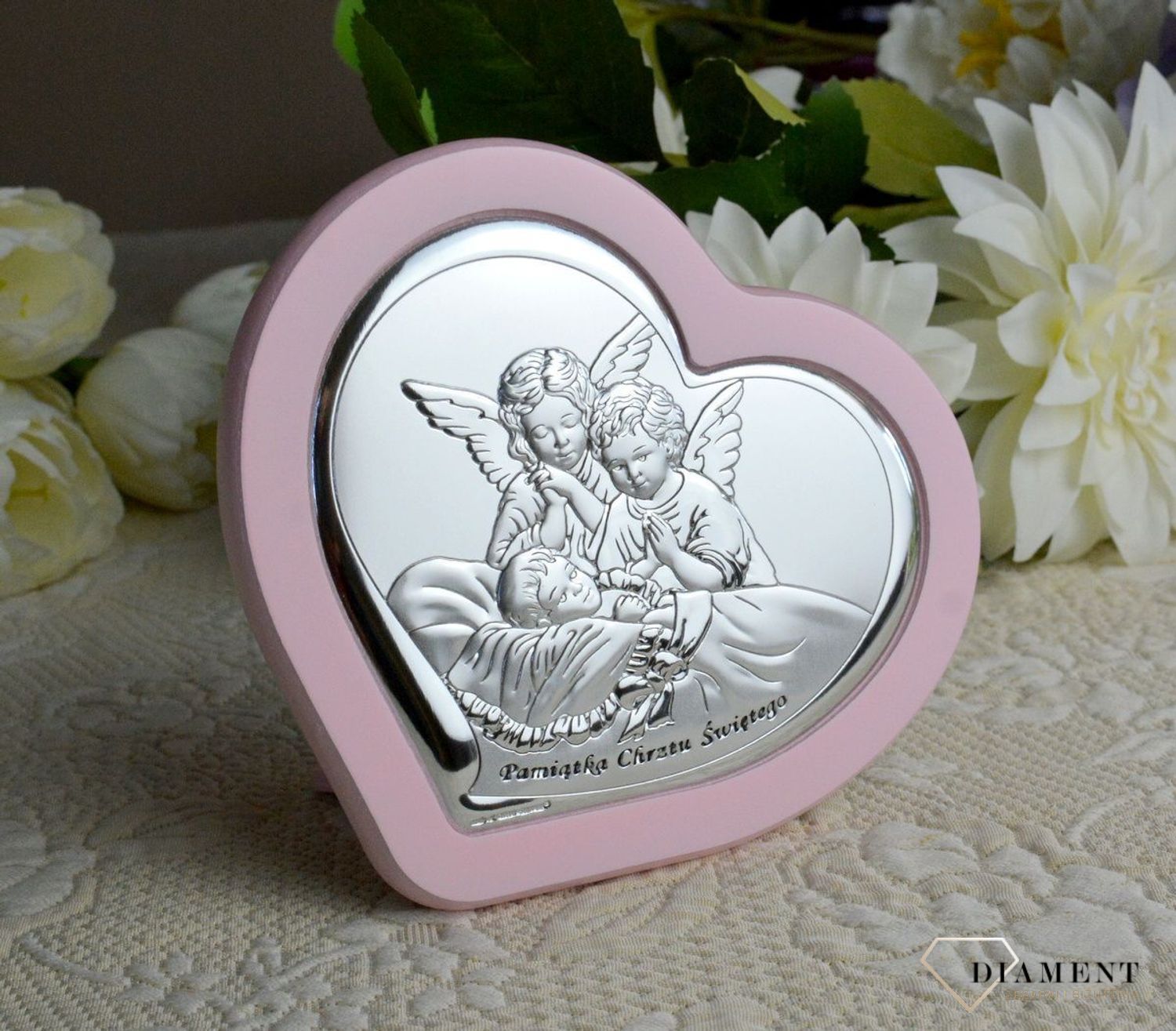 Uroczy obrazek w kształcie serca z wizerunkiem dwóch aniołków pochylających się nad dzieckiem. Wykonany z wysokiej jakości drewna oraz metalu laminowanego srebrem, dzięki któremu produkt zachowa swój blask.webp