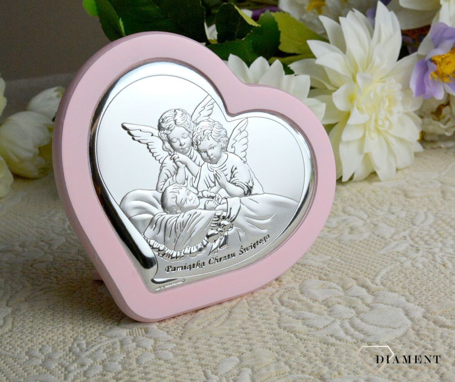 Uroczy obrazek w kształcie serca z wizerunkiem dwóch aniołków pochylających się nad dzieckiem. Wykonany z wysokiej jakości drewna oraz metalu laminowanego srebrem, dzięki któremu produkt zachowa swój blask.webp
