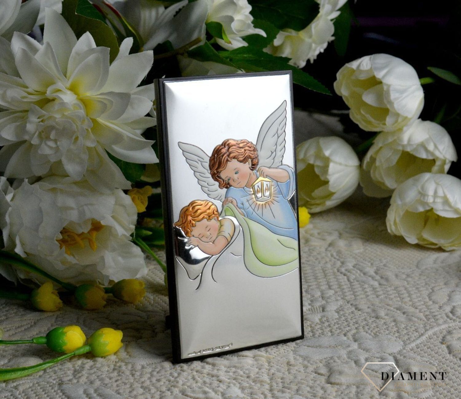 Obrazek srebrny z Aniołem Stróżem to piękna ozdoba dziecięcego pokoju. Pamiątka jest symbolicznym przedstawieniem opieki roztoczonej nad malcem przez Bożą Opatrzność..webp