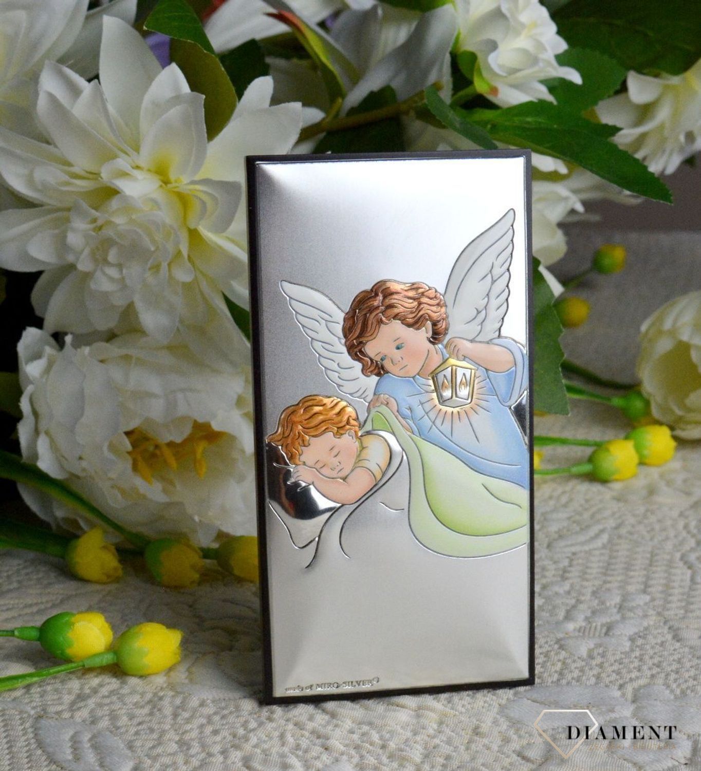 Obrazek srebrny z Aniołem Stróżem to piękna ozdoba dziecięcego pokoju. Pamiątka jest symbolicznym przedstawieniem opieki roztoczonej nad malcem przez Bożą Opatrzność..webp