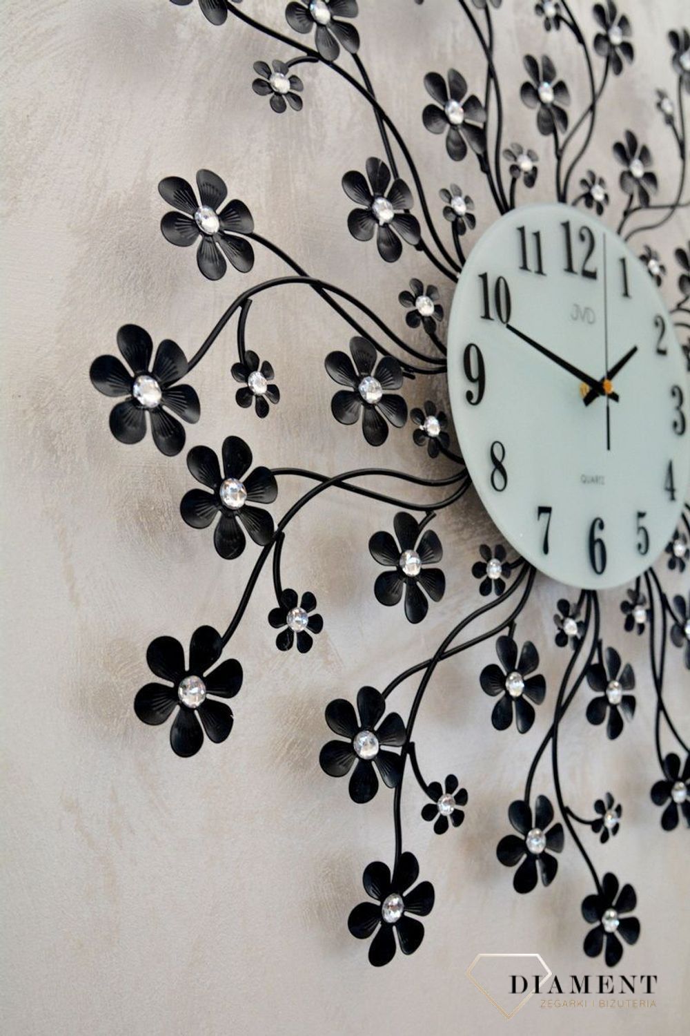 Zegar na ścianę nowoczesny z kryształkami JVD kwiatki HJ85.  Zegar ścienny JVD HJ85 wyposażony jest w kwarcowy mechanizm, zasilany za pomocą baterii. Posiada bardzo wysoką dokładność mierzenia czasu +- 10 sekund w przeciągu 30 dni..jpg
