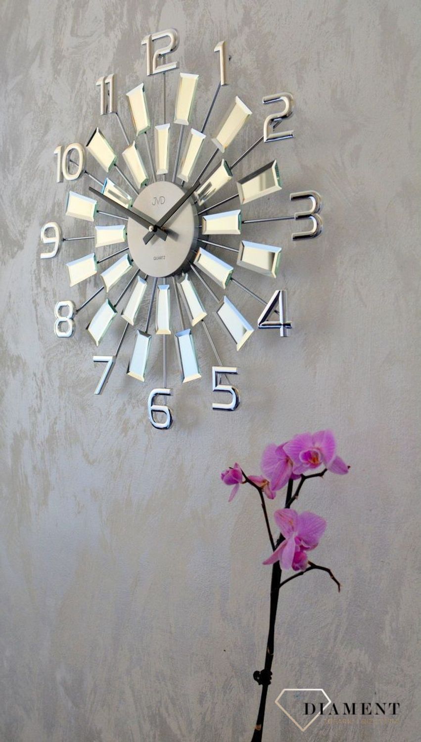Zegar ścienny 49 cm z kryształkami Cristal JVD HT100.3 wyposażony jest w kwarcowy mechanizm, zasilany za pomocą baterii. Posiada bardzo wysoką dokładność mierzenia czasu +- 10 sekund w przeciągu 30 dni..webp