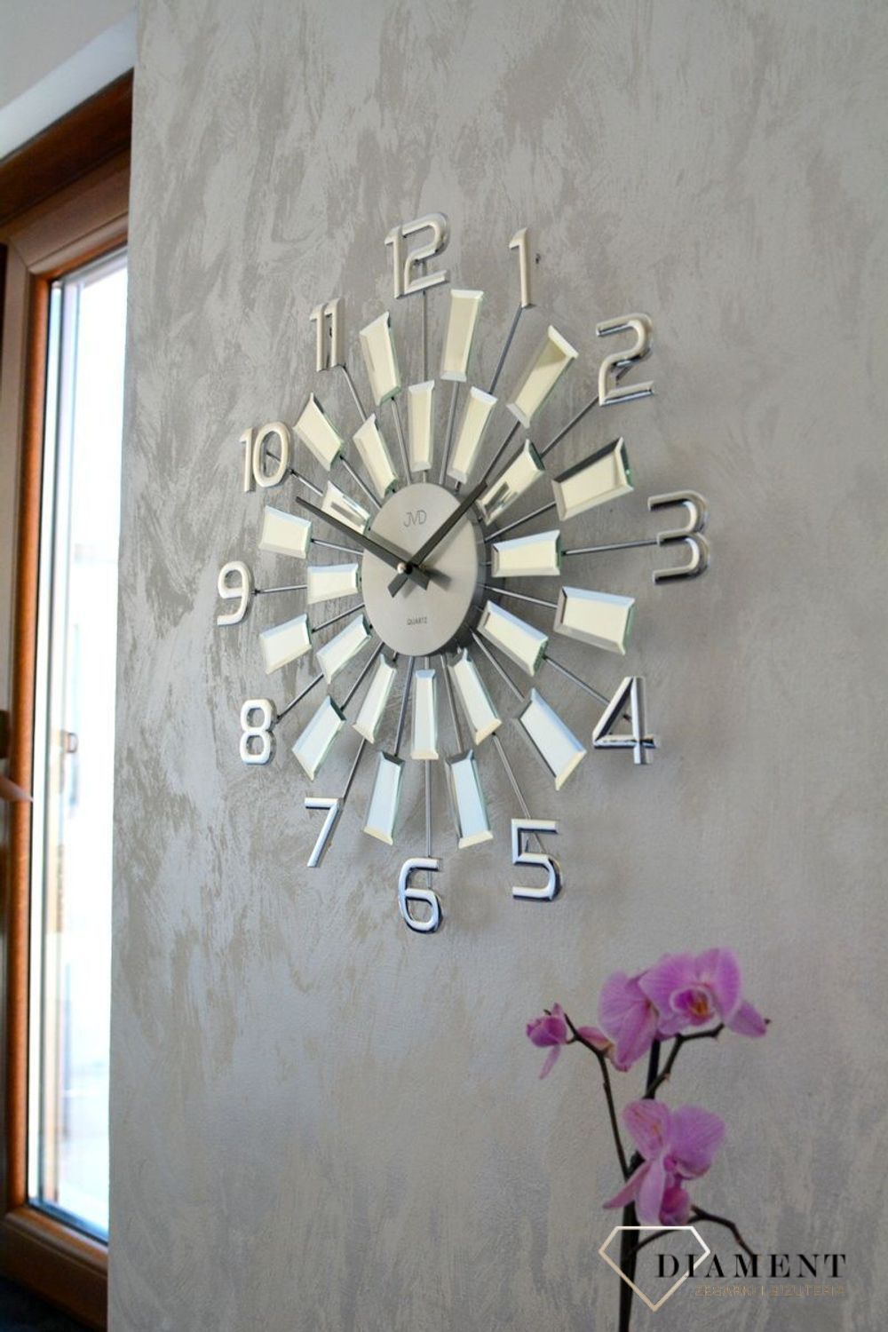 Zegar ścienny 49 cm z kryształkami Cristal JVD HT100.3 wyposażony jest w kwarcowy mechanizm, zasilany za pomocą baterii. Posiada bardzo wysoką dokładność mierzenia czasu +- 10 sekund w przeciągu 30 dni..webp