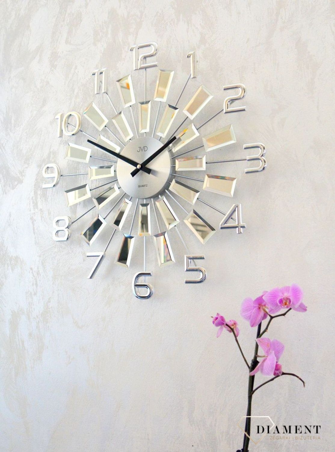 Zegar ścienny 49 cm z kryształkami Cristal JVD HT100.3 wyposażony jest w kwarcowy mechanizm, zasilany za pomocą baterii. Posiada bardzo wysoką dokładność mierzenia czasu +- 10 sekund w przeciągu 30 dni..webp