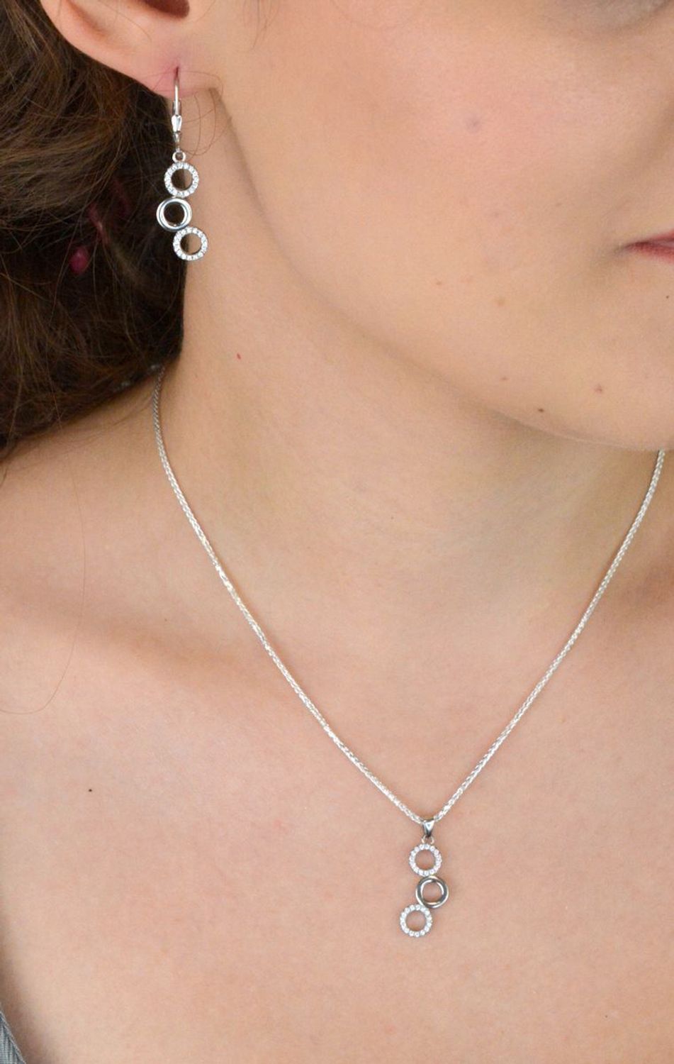 Elegancki srebrny komplet DIA-KPL-11828-925 z potrójnymi kółeczkami i błyszczącymi cyrkoniami. Kolczyki z wygodnym zapięciem na bigiel. Waga 4,60 g, długość kolczyków 3,8 cm, zawieszka 2,2 cm.3.jpg