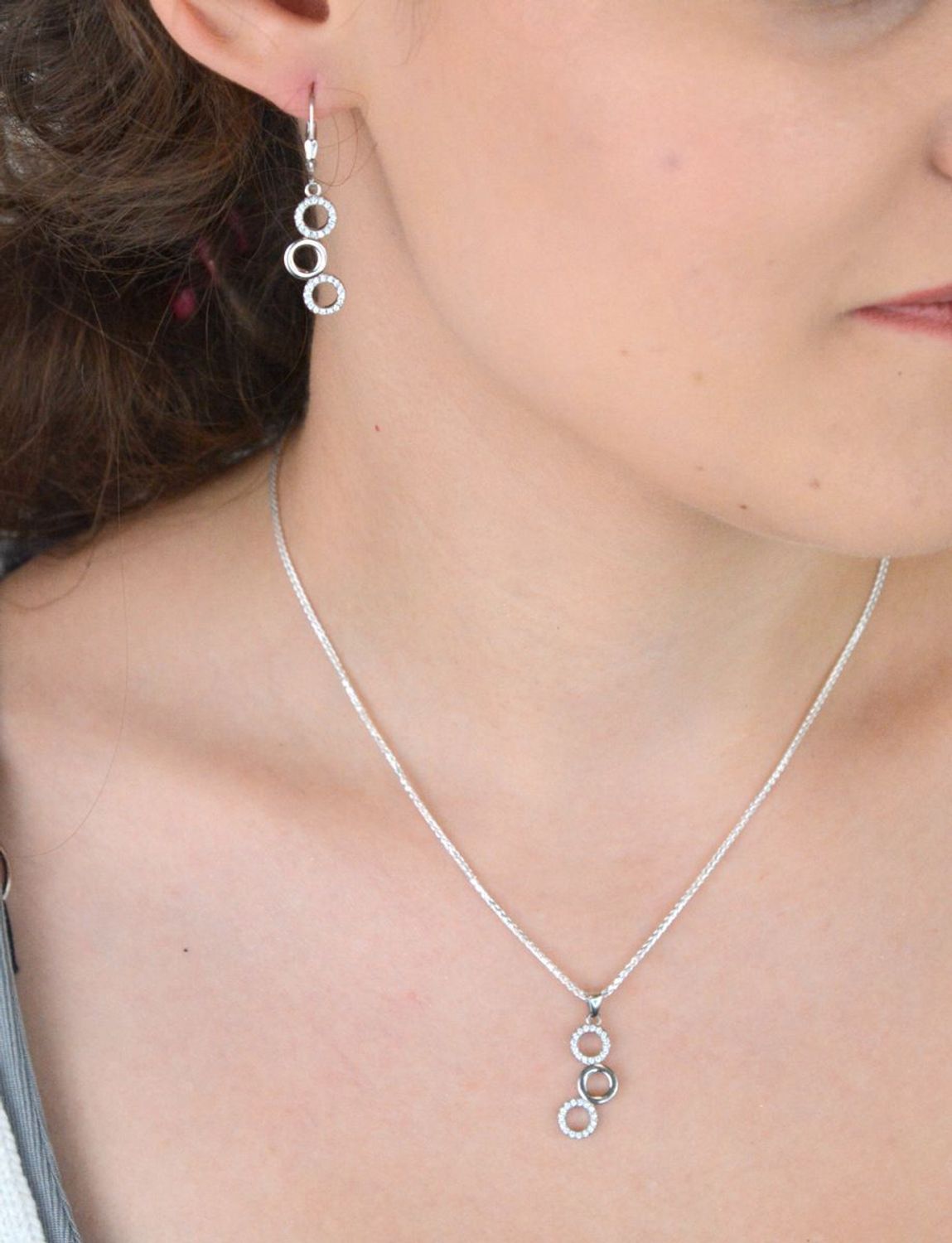 Elegancki srebrny komplet DIA-KPL-11828-925 z potrójnymi kółeczkami i błyszczącymi cyrkoniami. Kolczyki z wygodnym zapięciem na bigiel. Waga 4,60 g, długość kolczyków 3,8 cm, zawieszka 2,2 cm.3.jpg