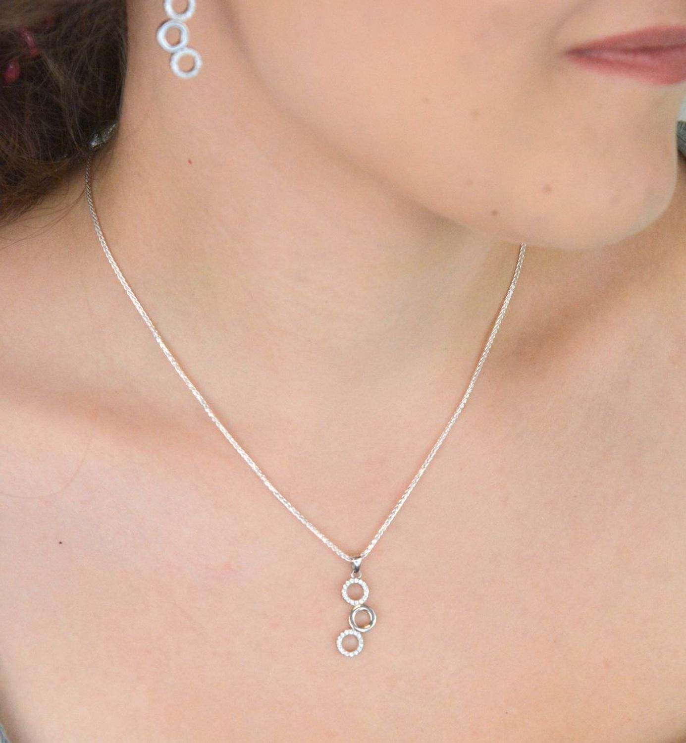 Elegancki srebrny komplet DIA-KPL-11828-925 z potrójnymi kółeczkami i błyszczącymi cyrkoniami. Kolczyki z wygodnym zapięciem na bigiel. Waga 4,60 g, długość kolczyków 3,8 cm, zawieszka 2,2 cm.3.jpg