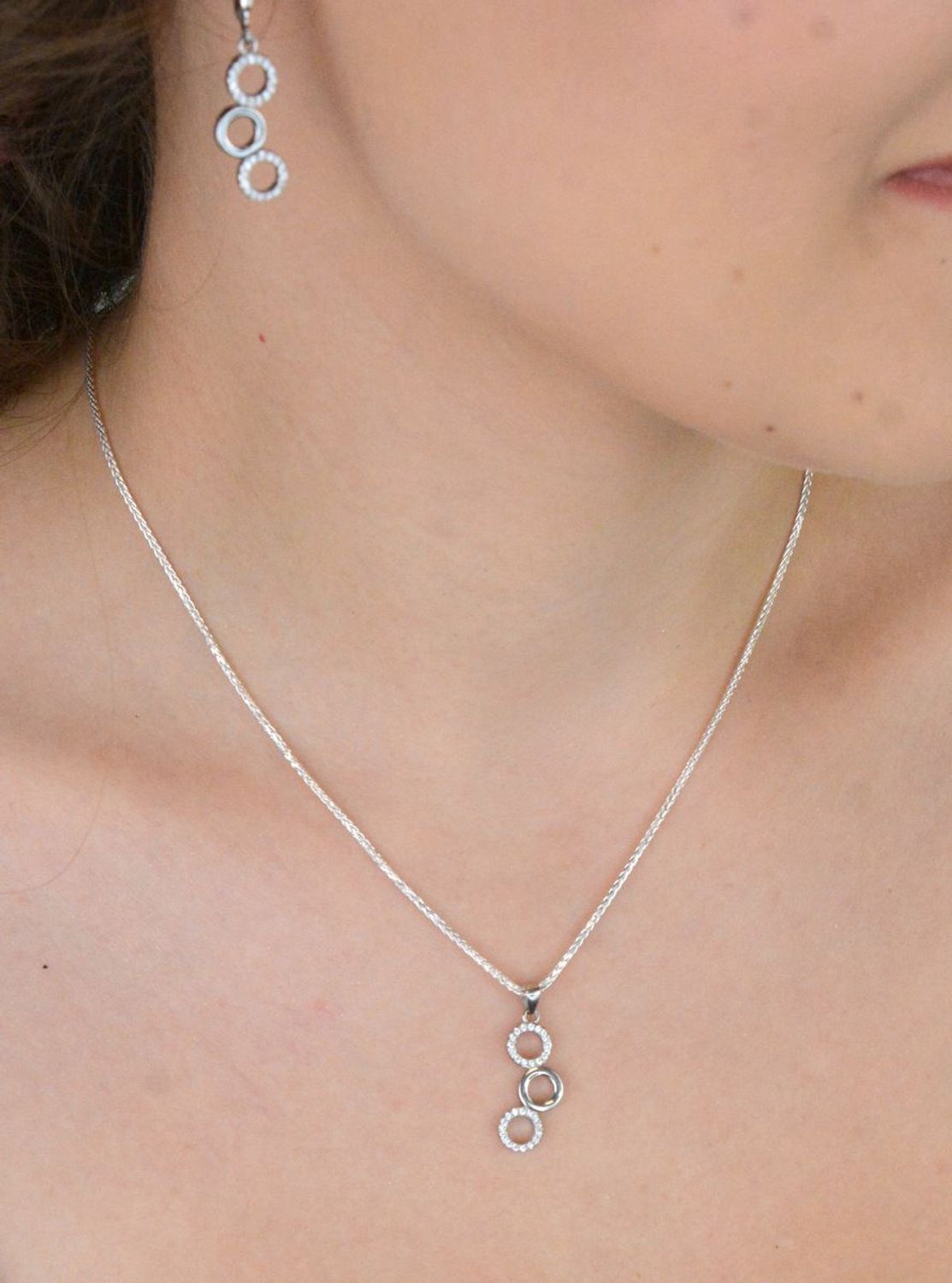 Elegancki srebrny komplet DIA-KPL-11828-925 z potrójnymi kółeczkami i błyszczącymi cyrkoniami. Kolczyki z wygodnym zapięciem na bigiel. Waga 4,60 g, długość kolczyków 3,8 cm, zawieszka 2,2 cm.3.jpg