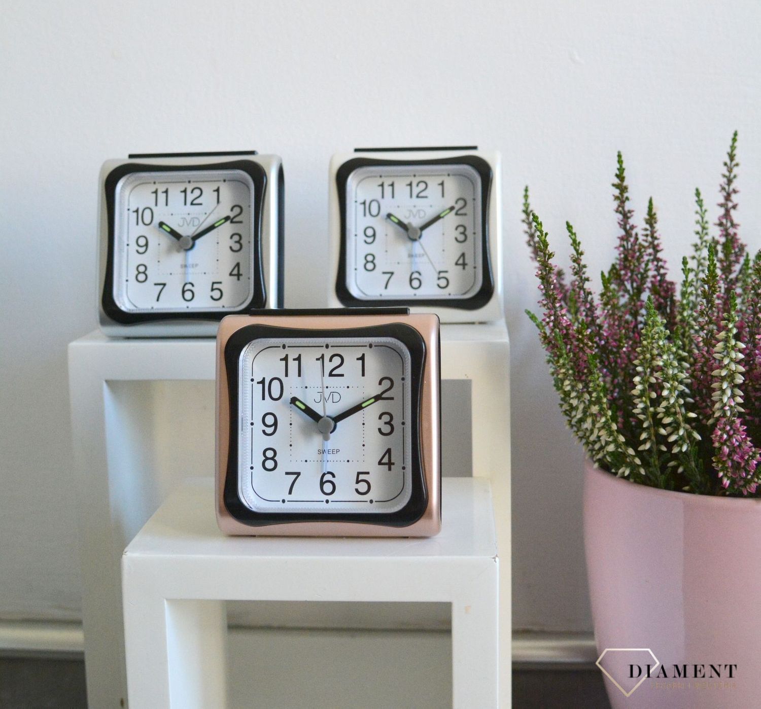 Budzik z wyraźną tarcza z czarnymi cyframi arabskimi. Budzik w obudowie w kolorze różowego złota..jpg