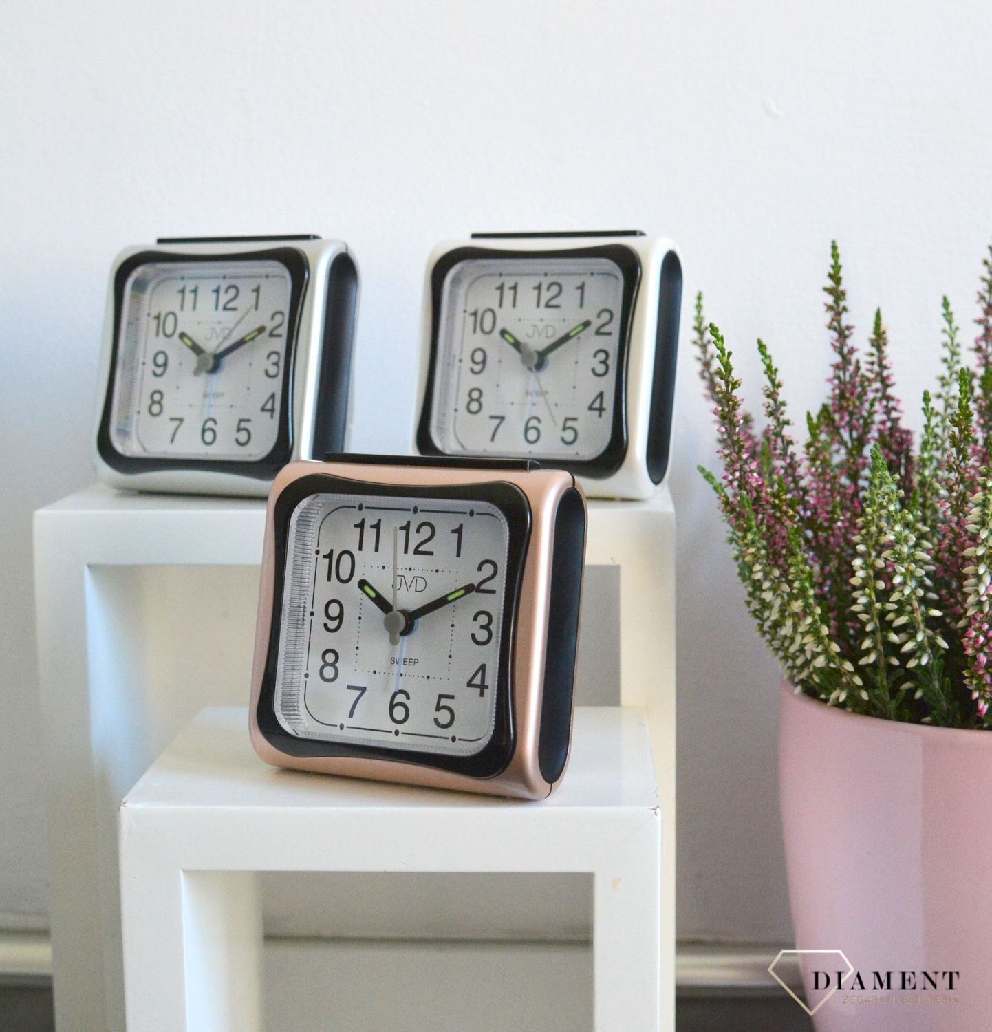 Budzik z wyraźną tarcza z czarnymi cyframi arabskimi. Budzik w obudowie w kolorze różowego złota..jpg