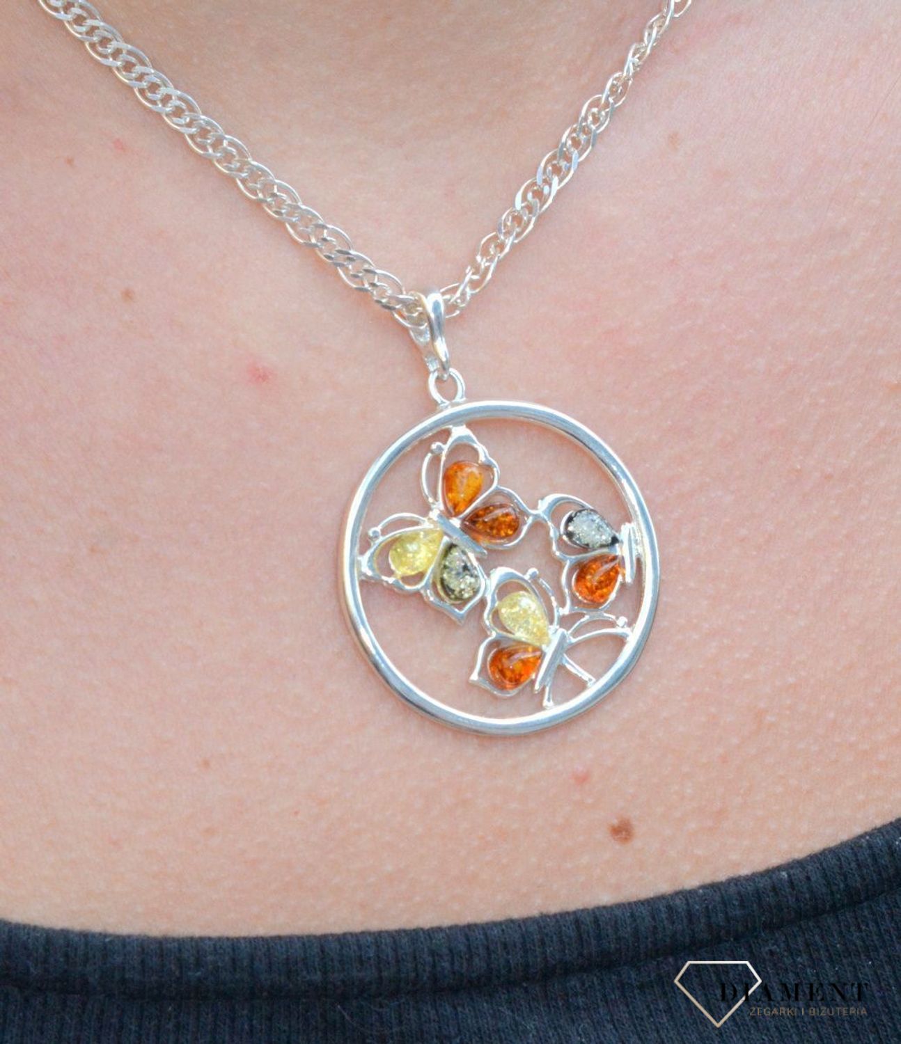 Zawieszka srebrna w kształcie koła z motylkami z bursztynu DIA-ZAW-7126-925. Bursztyn wprawiono w najwyższej jakości srebro o próbie 925, kruszec od wielu setek lat symbolizujący głębię emocjonalną, duchowość i żeńską energię.jpg