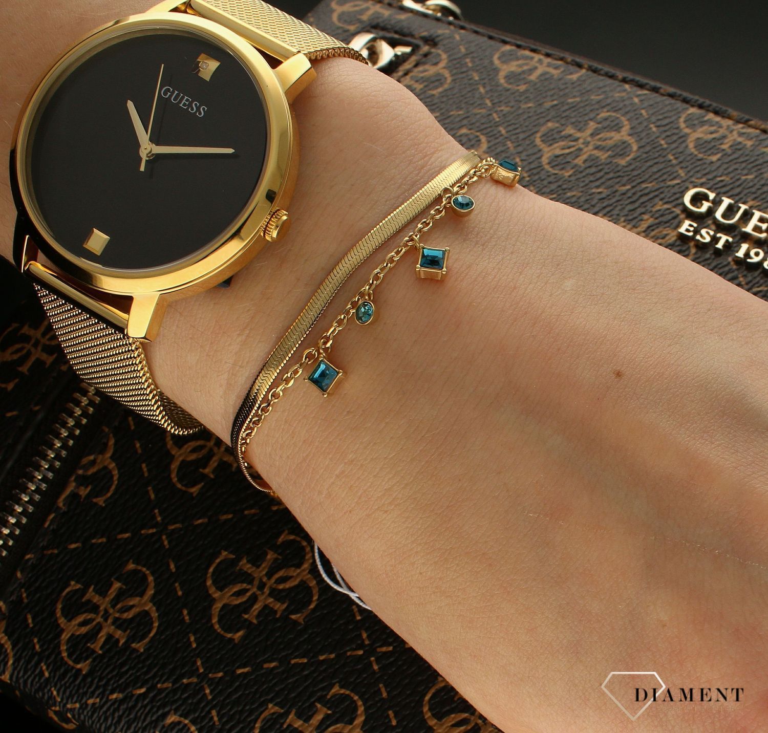 Bransoletka damska Guess z niebieskimi cyrkoniami JUBB03068JWYGAQS. Bransoletka damska Guess w złotym kolorze z wiszącymi elementami ozdobnymi w niebieskim kolorze. Stalowa bransoletka w kolorze złotym z cyrkoniami. Bransoletka Guess na pre.jpg