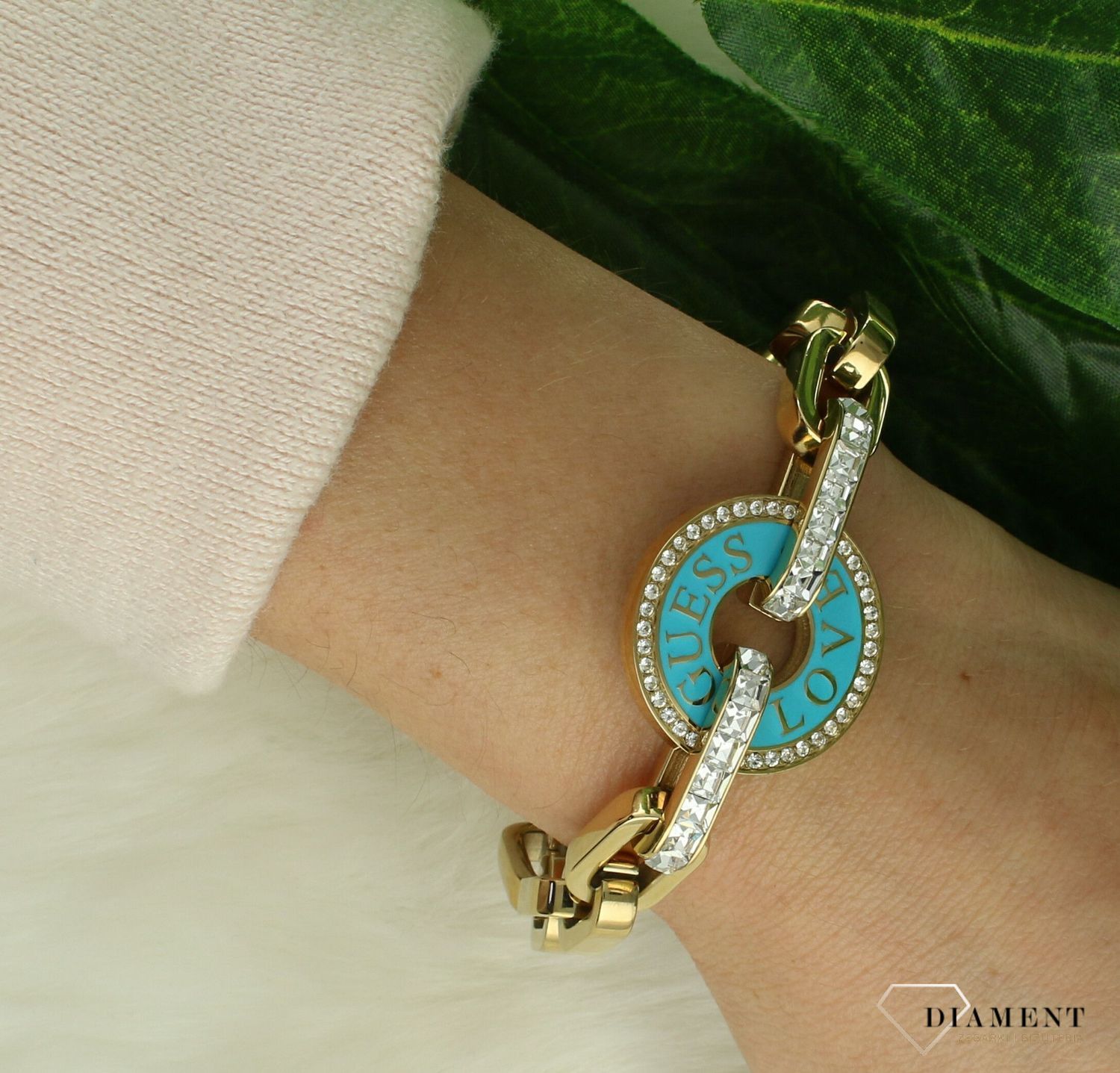 Bransoletka GUESS stalowa w kolorze złotym z elementem zdobnym JUBB04076JWYGTQS. Bransoletka wykonana z łańcuszka o splocie ankier z większymi ogniwami oraz zawieszką w kształcie koła z emalią w kolorze turkusowym z logo m.jpg
