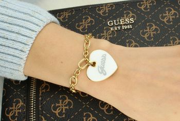 Bransoletka Guess z pozłacanej stali i zawieszką serce z białej emalii. Długość 18 cm + 3 cm. Elegancka, romantyczna biżuteria z logo Guess. Model JUBB05149JWYGWHS. Bransoletka damska Guess z białym sercem i poz.jpg
