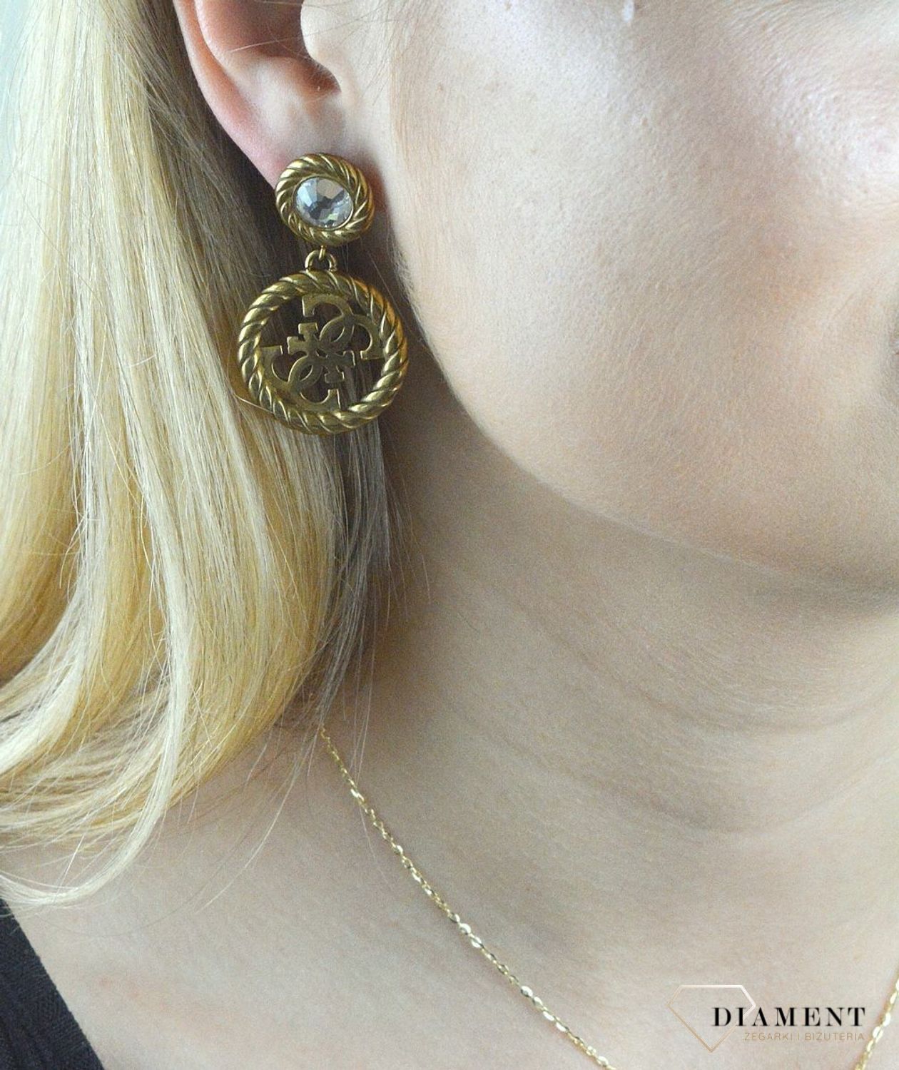 Kolczyki GUESS stalowe pozłacane z cyrkonią  JUBE01008JWAG. Stalowe kolczyki wiszące z logo marki GUESS w kolorze złotym ozdobione kryształami. Kolczyki składają się z kryształka do którego dołączony jest większy element w f (1).jpg