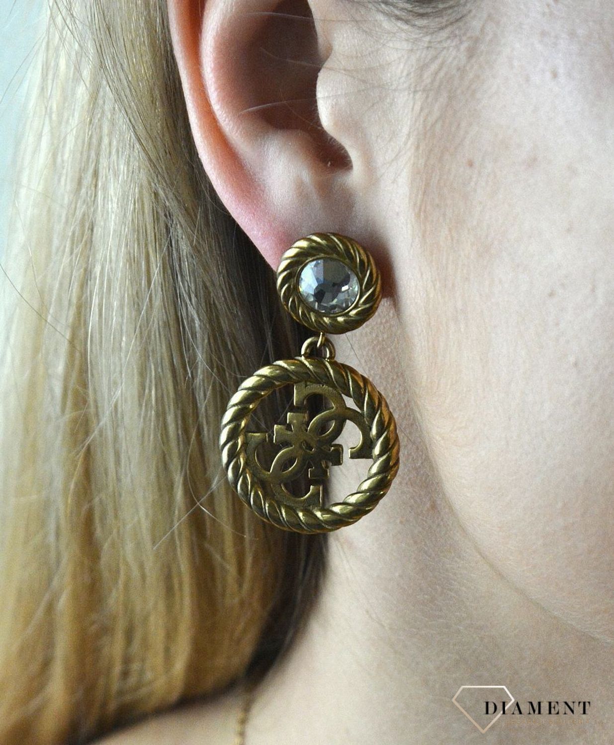 Kolczyki GUESS stalowe pozłacane z cyrkonią  JUBE01008JWAG. Stalowe kolczyki wiszące z logo marki GUESS w kolorze złotym ozdobione kryształami. Kolczyki składają się z kryształka do którego dołączony jest większy element w f (1).jpg