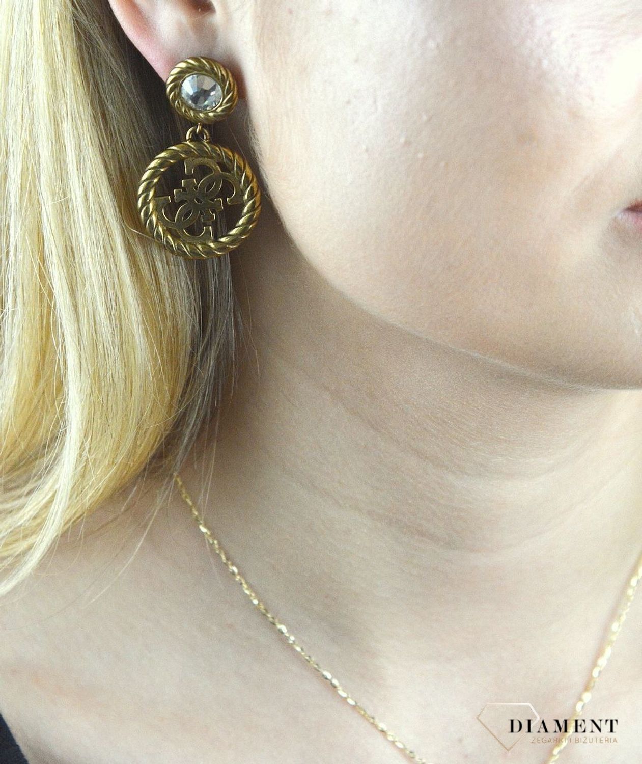 Kolczyki GUESS stalowe pozłacane z cyrkonią  JUBE01008JWAG. Stalowe kolczyki wiszące z logo marki GUESS w kolorze złotym ozdobione kryształami. Kolczyki składają się z kryształka do którego dołączony jest większy element w f (1).jpg