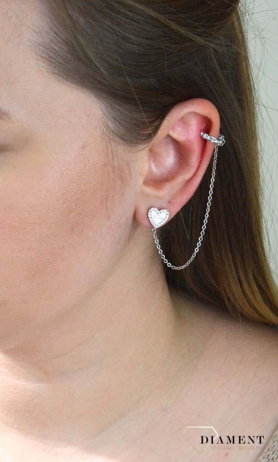 Nausznica srebrna GUESS z łańcuszkiem i kolczykami  JUBE01080JWRHTU. Nausznica w kolorze srebra GUESS z łańcuszkiem i kolczykami w kształcie serca. Stalowe kolczyki z motywem serca ozdobione błyszczącymi kryształami.jpg