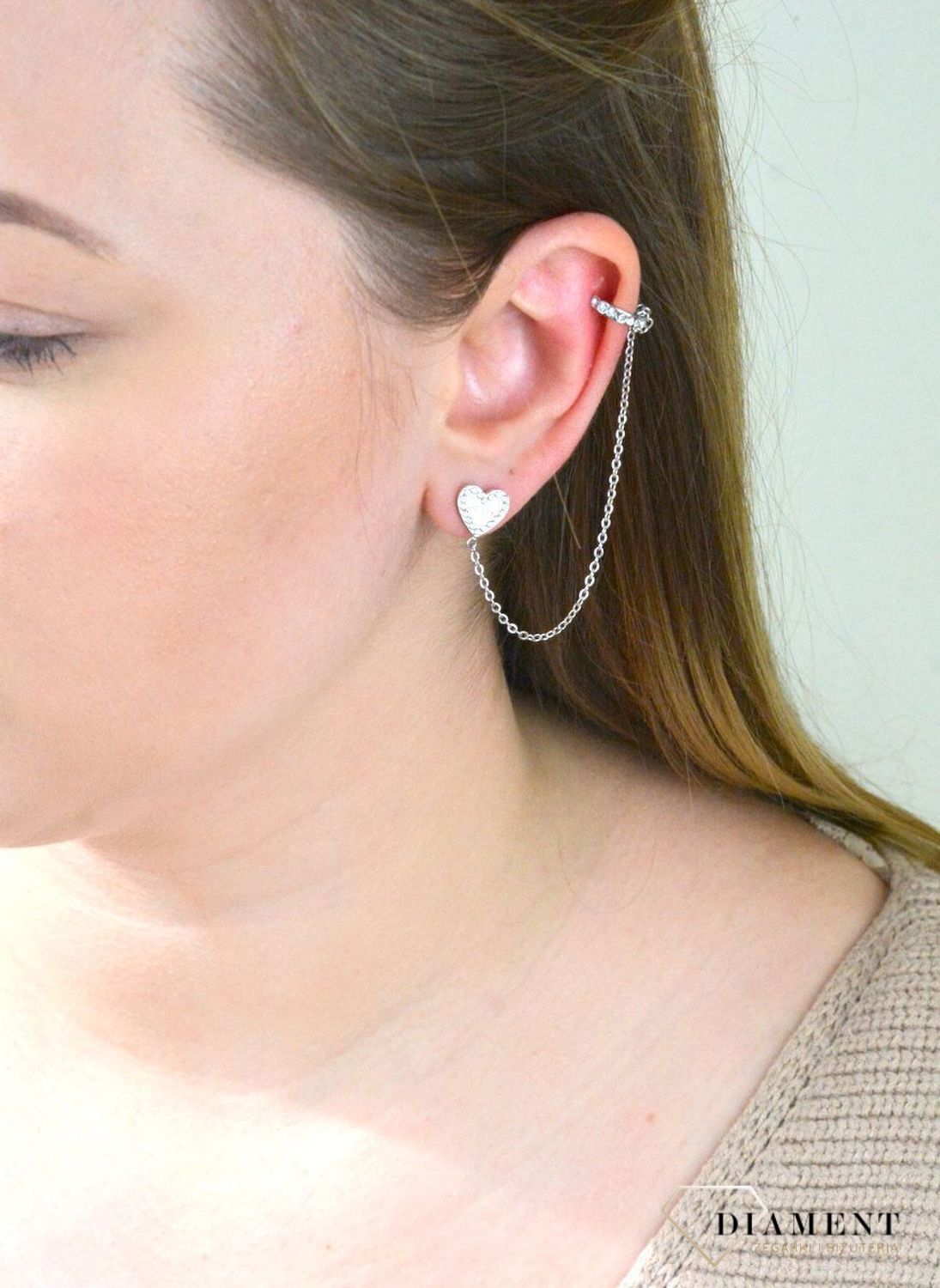 Nausznica srebrna GUESS z łańcuszkiem i kolczykami  JUBE01080JWRHTU. Nausznica w kolorze srebra GUESS z łańcuszkiem i kolczykami w kształcie serca. Stalowe kolczyki z motywem serca ozdobione błyszczącymi kryształami.jpg