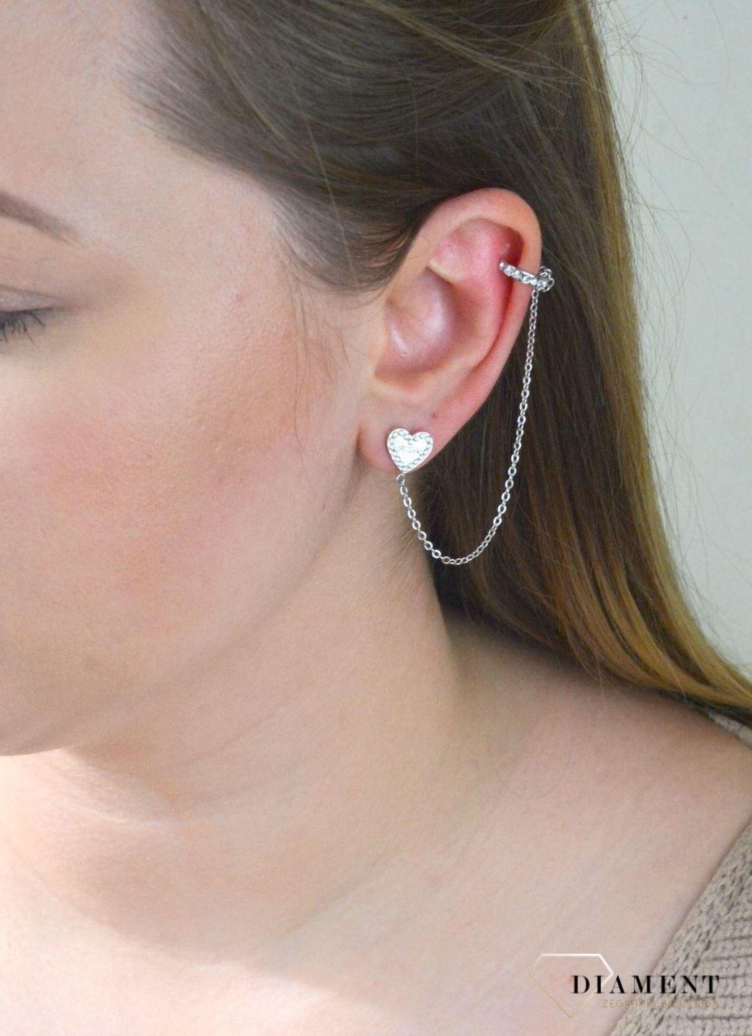 Nausznica srebrna GUESS z łańcuszkiem i kolczykami  JUBE01080JWRHTU. Nausznica w kolorze srebra GUESS z łańcuszkiem i kolczykami w kształcie serca. Stalowe kolczyki z motywem serca ozdobione błyszczącymi kryształami.jpg