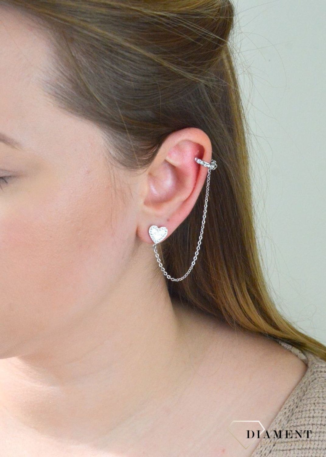 Nausznica srebrna GUESS z łańcuszkiem i kolczykami  JUBE01080JWRHTU. Nausznica w kolorze srebra GUESS z łańcuszkiem i kolczykami w kształcie serca. Stalowe kolczyki z motywem serca ozdobione błyszczącymi kryształami.jpg