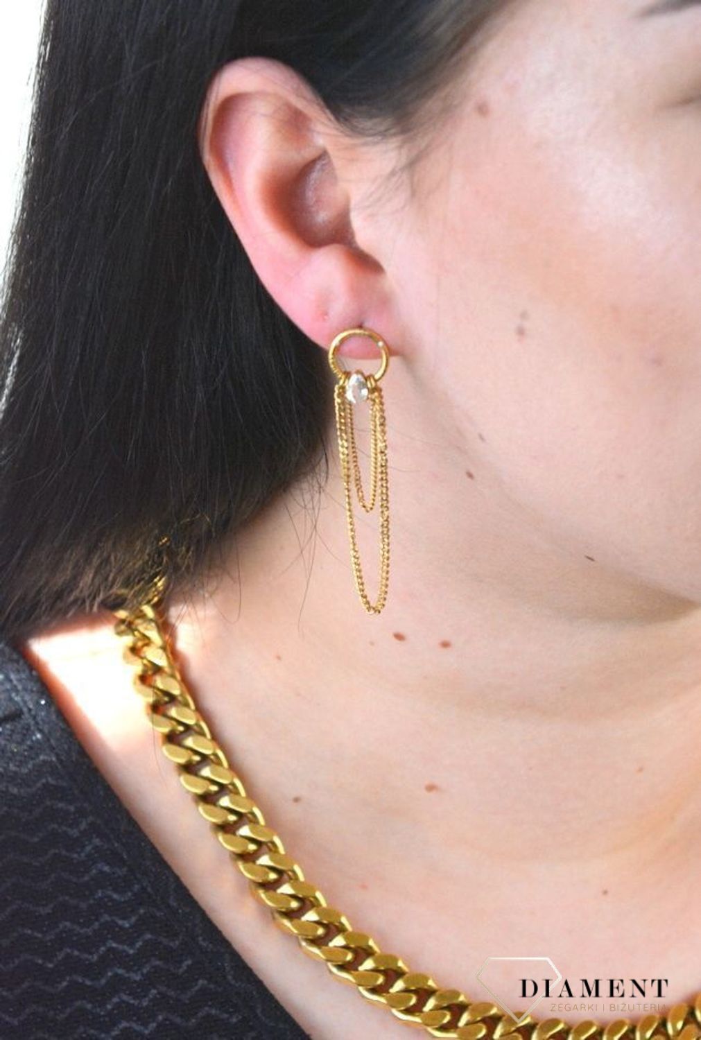 Stalowe kolczyki wiszące z logo marki GUESS w kolorze złotym. Kolczyki składają się z łańcuszków pancerki do którego dołączony jest kryształka..jpg