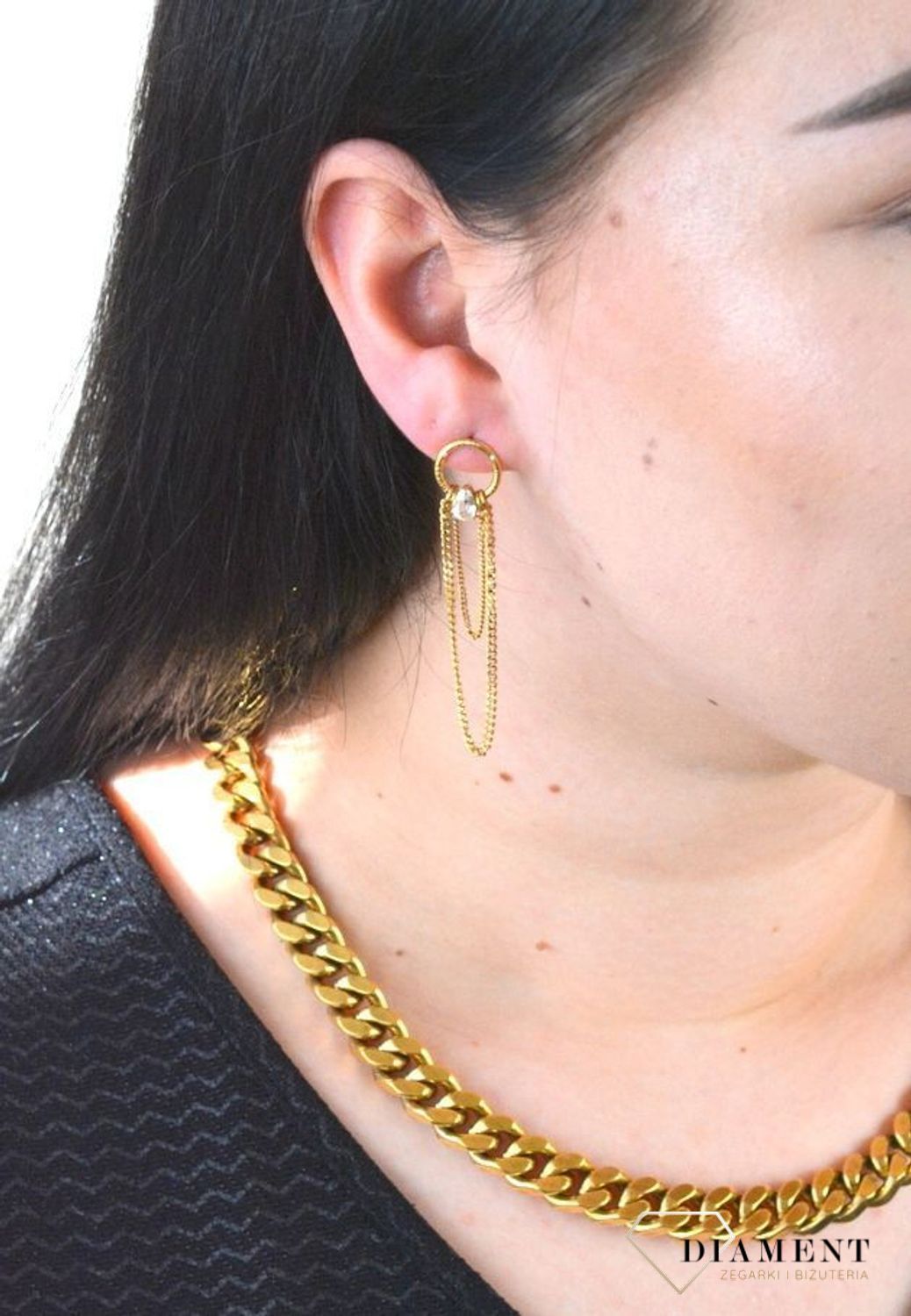 Stalowe kolczyki wiszące z logo marki GUESS w kolorze złotym. Kolczyki składają się z łańcuszków pancerki do którego dołączony jest kryształka..jpg