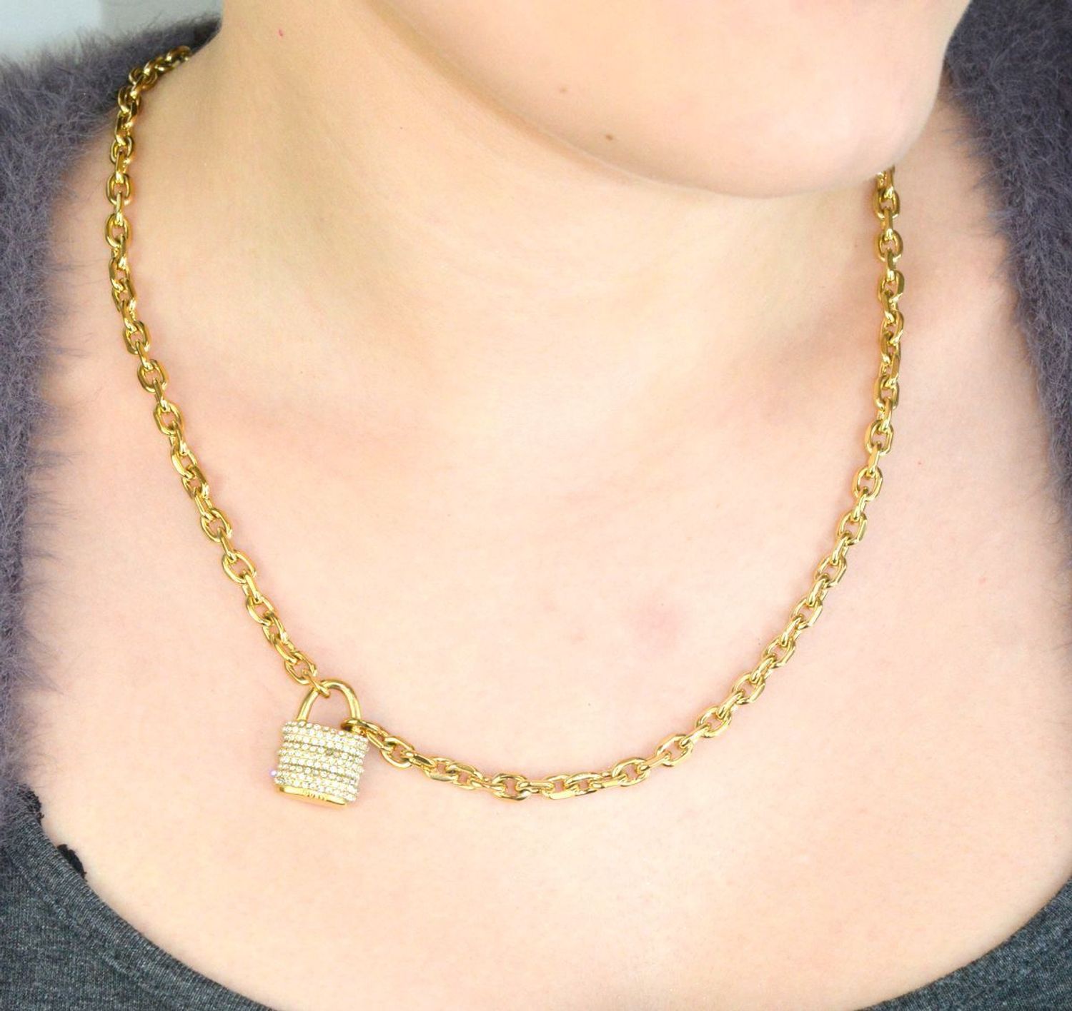 Pozłacany naszyjnik GUESS JUBN05415JWYGTU z zawieszką w kształcie kłódki i zdobieniem z kamieni. Wykonany ze stali szlachetnej, łączy elegancję i trwałość. Idealny na co dzień i wyjątkowe 1.jpg