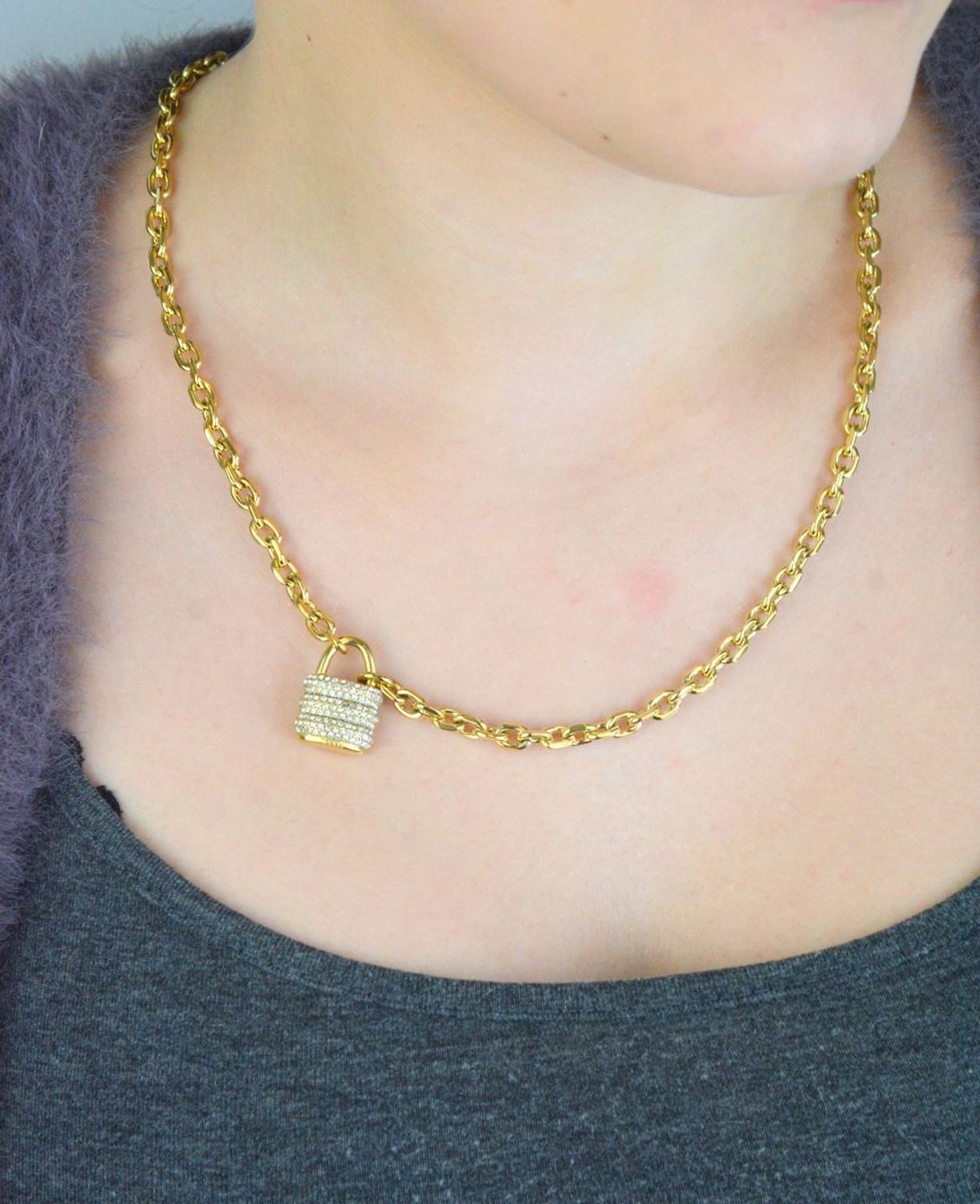 Pozłacany naszyjnik GUESS JUBN05415JWYGTU z zawieszką w kształcie kłódki i zdobieniem z kamieni. Wykonany ze stali szlachetnej, łączy elegancję i trwałość. Idealny na co dzień i wyjątkowe 1.jpg