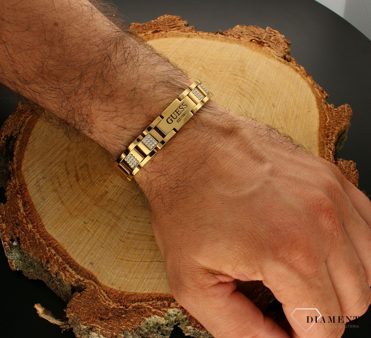 Bransoletka męska GUESS stalowa w kolorze złotym JUMB01342JWYG. Bransoletka GUESS z logo po środku ozdobiona cyrkoniami. Bransoletka, która świetnie się sprawdzi jako dodatek do stylizacji.webp